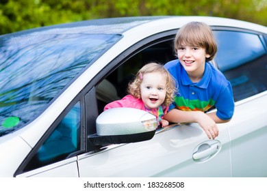 Two Kids, School Age Boy And Cute Curly Toddler Girl, Enjoy Vacation Car Ride On A Summer Weekend Watching Out Of Window Of Silver Color Modern Family Vehicle After Rain With Drops On Wet Front 