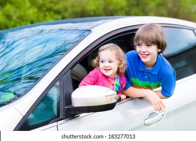 Two Kids, School Age Boy And Cute Curly Toddler Girl, Enjoy Vacation Car Ride On A Summer Weekend Watching Out Of Window Of Silver Color Modern Family Vehicle After Rain With Drops On Wet Front 