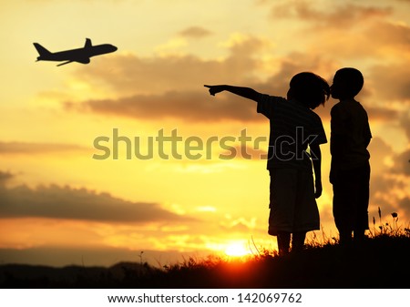 Two kids silhouette on meadow looking at airplane in air