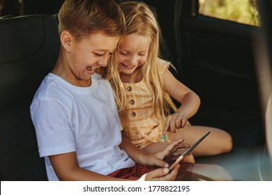 Two Kids Sitting On Backseat Of Car Playing Games On A Digital Tablet. Traveling In A Car.