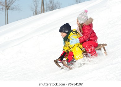 Two Kids Sliding With Sledding In The Snow.