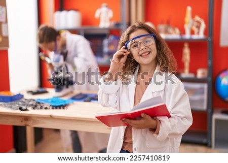 Two kids students using microscope reading notebook at laboratory classroom