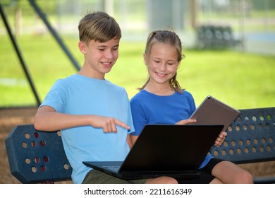 Two kids, teenager boy holding laptop computer and pretty young girl with digital tablet studying together outdoors sitting on bench. Education during quarantine concept - Powered by Shutterstock