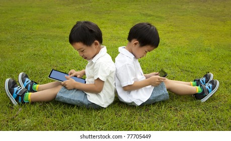 Two Kids Using Touchscreen Tablet PC On The Grass