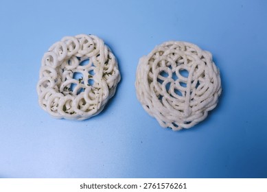 Two knotted, off-white fiber objects rest on a smooth blue surface. Their interwoven patterns form circular, organic shapes. Each structure displays a unique, handcrafted texture and form