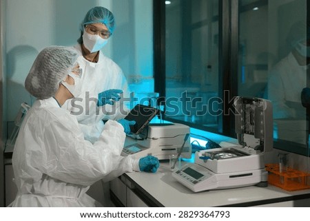 Two lab technicians in protective suits operate a moisture analyzer and tablet in a sterile lab, ideal for pharmaceutical and food quality control concepts.