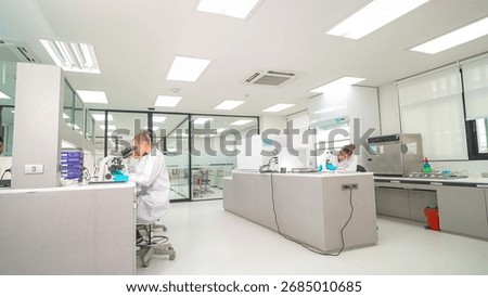 Two laboratory technicians are working diligently in a well-lit, modern lab. One is seated, analyzing data, while the other prepares samples, surrounded by advanced equipment and a clean workspace.