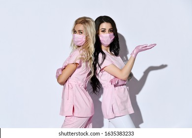 Two ladies in pink scrubs, disposable gloves and medical masks are posing isolated on white. Medical staff, cosmetologist, tattoo artist, hairdresser. Beauty. Copy space, advertising area. Close up