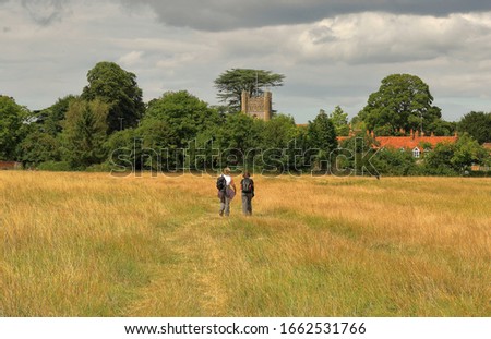 Two lady Ramblers on a path through a field approaching and English village