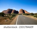 Two lane road in Uluru Kata Tjuta National Park, Australia with Mount Olga in the distance.