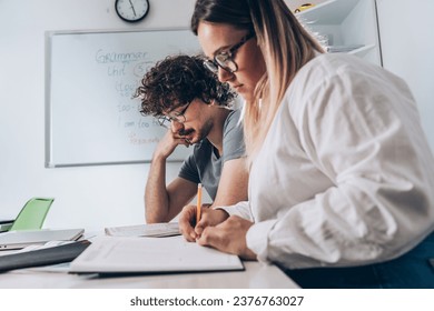 Two language learning students are focused on taking a test in their language class, showcasing their dedication to mastering a foreign tongue.