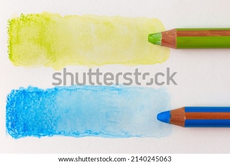 Two large colored green and blue pencils and water-bleached stripes. Testing watercolor pencils