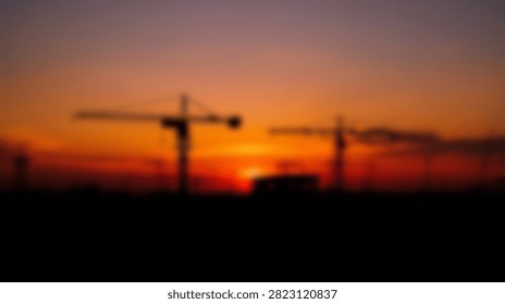 Two large construction cranes are silhouetted against a dramatic and colorful sunset sky, symbolizing progress and development.