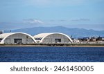 Two Large Hangar Buildings Near a Ramp Full of Helicopters Near the Shore