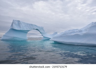 Two Large Icebergs In Antarctica At Eye-level As Seen From A Small Boat.  Gorgeous Aquamarine Blue Coloring Where Iceberg Is Visible Below Water. Cloudy Skies.