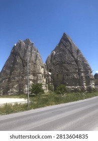 Two large, pointed rock formations in Cappadocia, Turkey, stand adjacent to a road