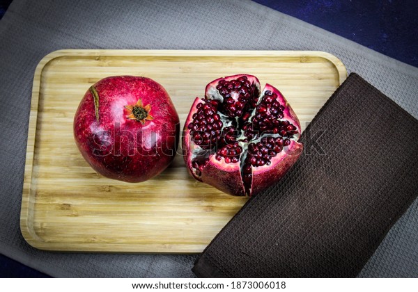 Two\
large large red pomegranate fruits. Whole red ripe pomegranate.\
Pomegranate fruit open which is divided into five parts which are\
held together on wooden tray on blue\
background.