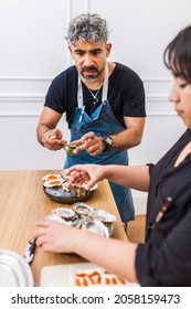 Two Latin Cooks Preparing Oysters During Private Dinner At Home. Professional Chef Preparing Food In The Kitchen With His Female Assistant.