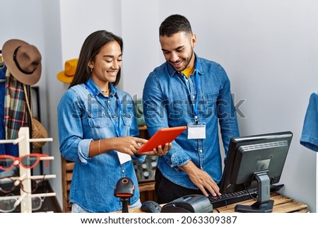 Two latin shopkeepers using touchpad working at clothing store.