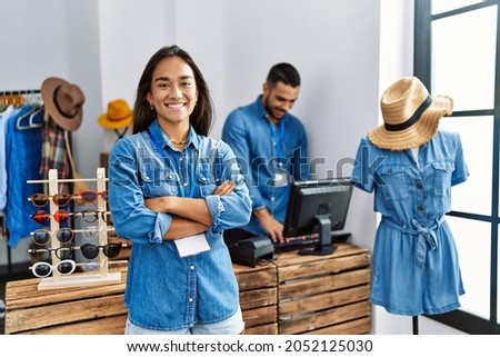 Two latin shopkeepers working at clothing store. Woman smiling happy standing with arms crossed gesture.