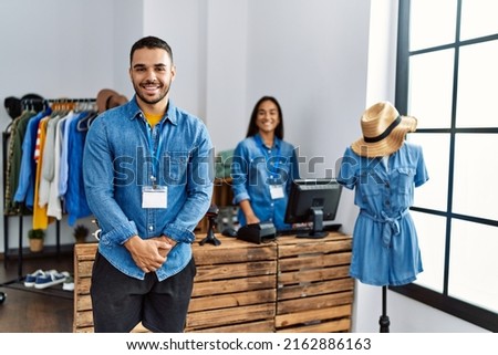 Two latin shopkeepers working at clothing store. Man smiling happy standing.