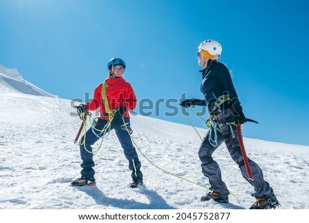 Two laughing to each other young women Rope team ascending Mont blanc du Tacul summit 4248m dressed mountaineering clothes with ice axes on snowy slopes. People extreme activities sporty concept image