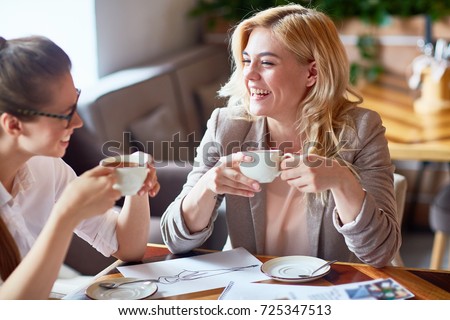 Two laughing girls having tea and discussing new creative project in cafe