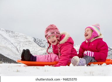 Two laughing kids sledding with a mountain scene in background