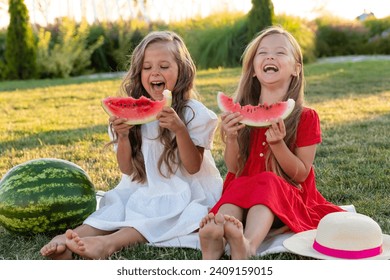 Two laughing merrily little girls two sisters eating watermelon on the lawn. picnic in the park. happy childhood. space for text. High quality photo - Powered by Shutterstock