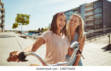 Two laughing young best friends having fun together while walking with a bicycle through the city in summer