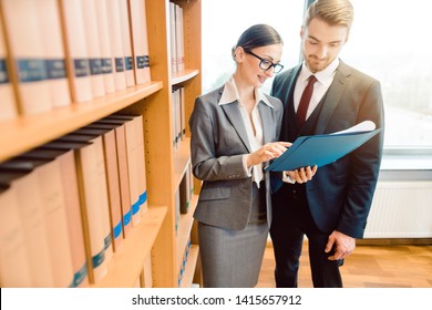 Two Lawyers In Library Of Law Firm Discussing Strategy In A Case Holding File 