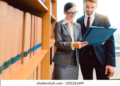 Two Lawyers In Library Of Law Firm Discussing Strategy In A Case Holding File