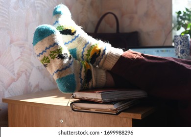 two legs in knitted woolen white and blue warm socks on a desk lying on two notebooks