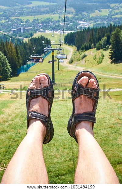 two legs in sandals against the backdrop of the\
mountains and cable car