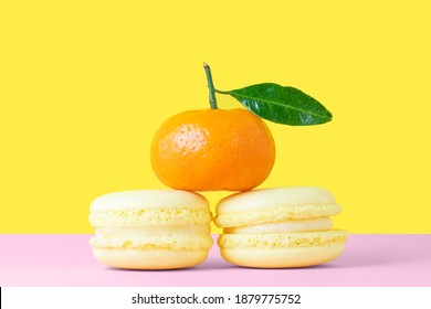 Two lemon French macarons with orange tangerine on a pink and yellow background in the form of a pyramid. Valentine's day gift