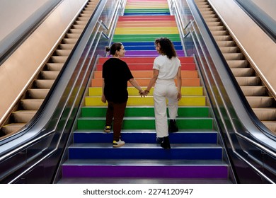 two lesbian girls in love climb the stairs in the colors of the lgtb flag on gay pride day - Powered by Shutterstock