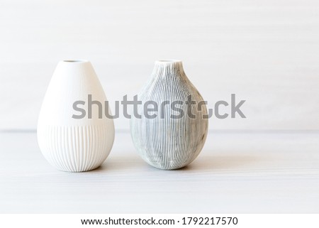 Two light clay vases on a white wooden shelf. 