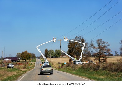 Two Linemen Stand In Cherry Pickers Working On Telephone Lines In Rural Arkansas.  Car Has Slowed To Go Around Equipment.