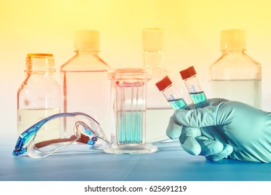 Two liquid samples in plastic vials in the hand of female scientist, scientific background in blue and orange