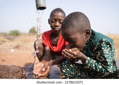 Two little african boys refresh themselves at the village fountain on a sizzling hot day