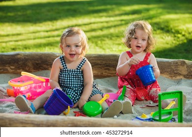 The Two Little Baby Girls Two-year Old Playing Toys In Sand Against Green Grass