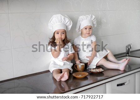 two little baker girls are drinking tea with a pabcakes in the kitchen