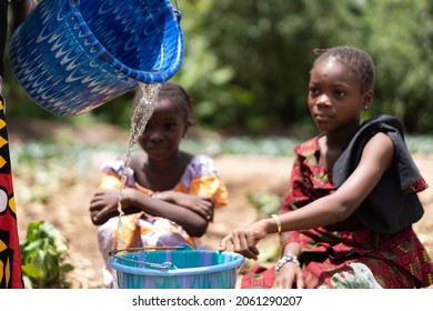 Two little black African girls crouched down at the village well waiting for their bucket to be filled with clean drinking water