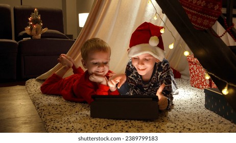 Two little boy having video talk on tablet computer while lying on floor in living room decorated for Christmas. Talking to their grandmother on winter holidays - Powered by Shutterstock