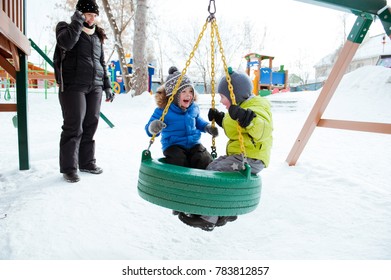 Two little boy ride on a swing on the Playground in winter. - Powered by Shutterstock