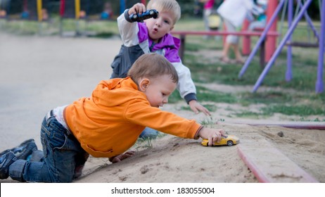 Two Little Boys Crawling On The Ground Playing With Toy Cars At A Childrens Playground