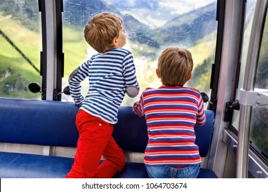 Two Little Boys Sitting Inside Of Cabin Of Cable Car And Looking On Mountains Landscape.