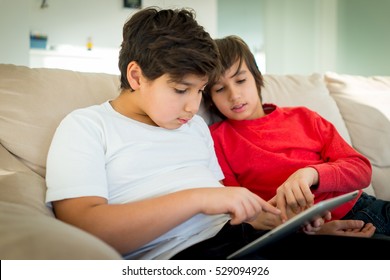 Two little boys sitting on sofa and working on tablet