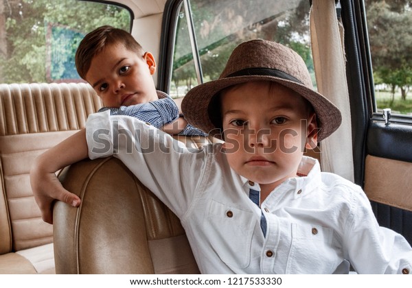 Two little boys in vintage clothes are sitting in a\
retro car