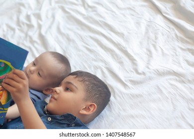 Two Little Brothers Reading A Book. Infant Kids Lying On The Bed And Read The Tale Before Sleeping. Reading A Short Story For Kids. Middle Eastern Children On Their Bed. Copy Space